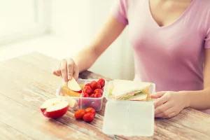 A woman eating a packed lunch of a sandwich, tomatoes, apples